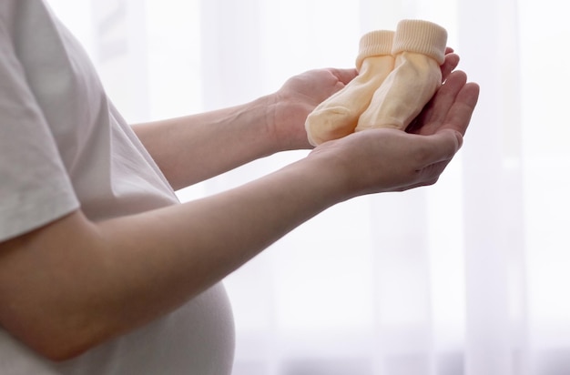 A pregnant girl in the later stages holds baby socks in her hands