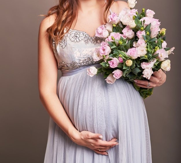 Pregnant girl on a light background with flowers. Photo without a face in the frame.