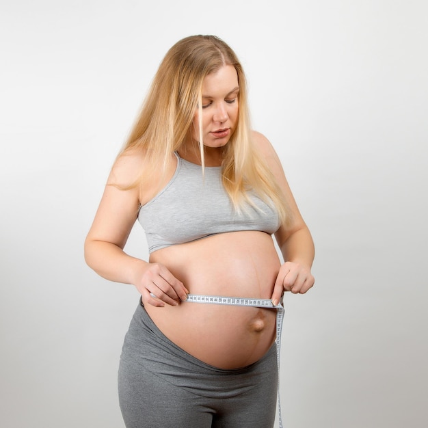 A pregnant girl measures her stomach with a tapeline Tracking the growth progress of the abdomen and baby