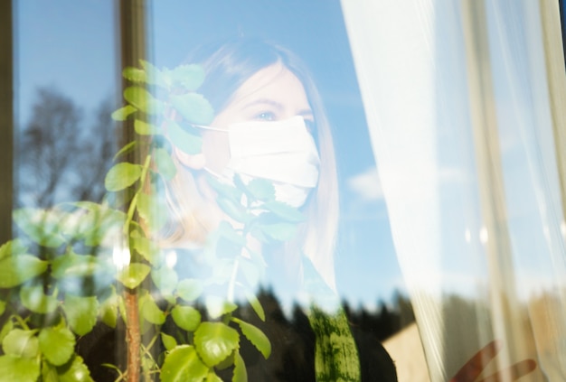 Photo pregnant girl in a medical mask looks out the window in covid-19 pandemic