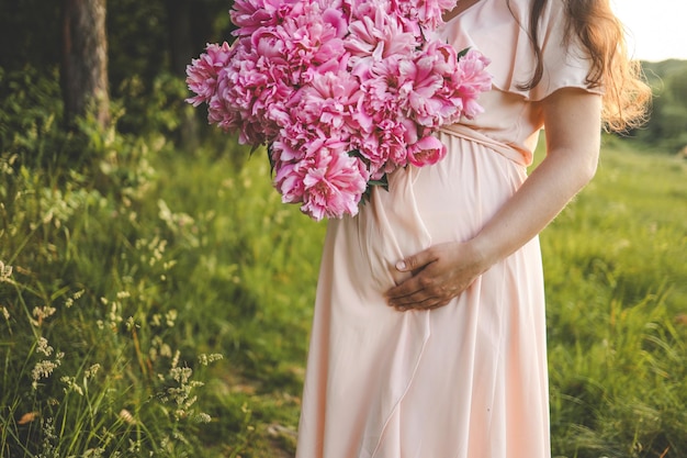 Pregnant girl in nature with a bouquet of peonies