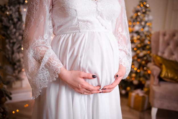 A pregnant girl at a New Year's photo session White long dress Many lights from the garland