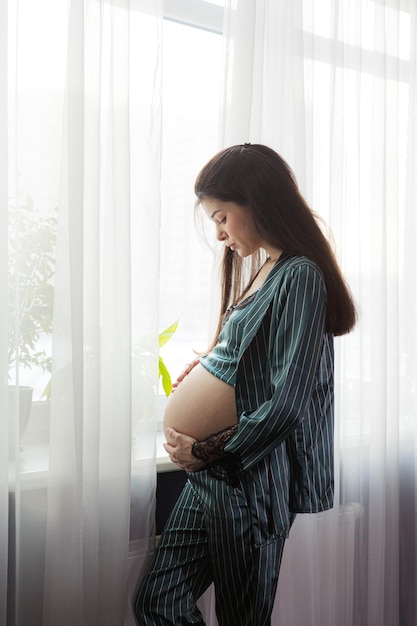 窓際に立っているパジャマ姿の妊婦