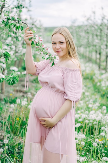 Pregnant girl in a pink dress in a flower garden