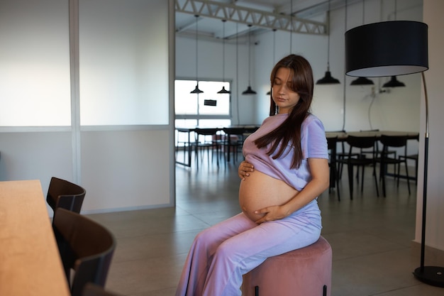 A pregnant girl sits on ottoman in spacious room meeting room