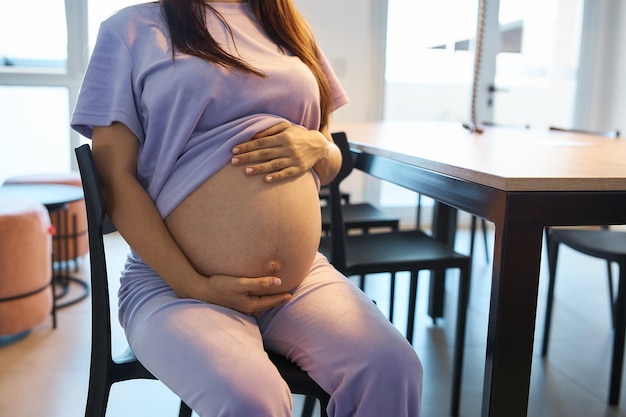 写真 彼女の胃のコワーキングに触れる大きなホールで椅子に座っている妊娠中の女の子