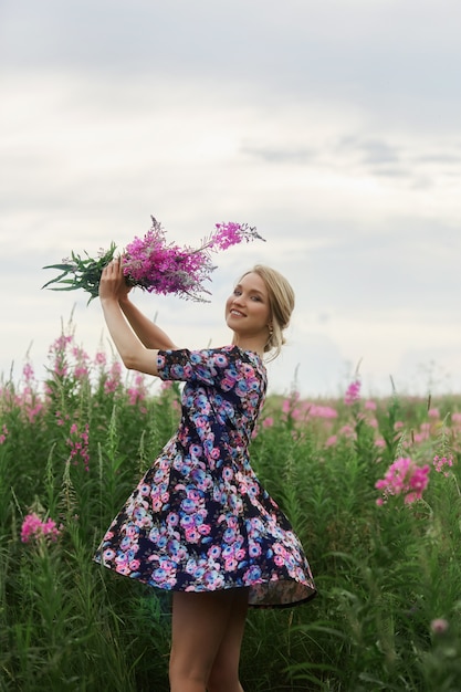 妊娠中の女の子が花ヤナギラン、笑みを浮かべて、花を摘む女性のフィールドを歩きます。