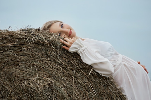 Pregnant girl walks in a field near haystacks in a long white dress