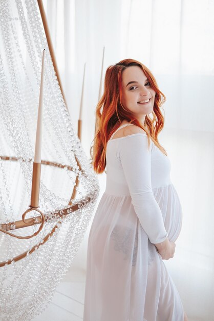 Pregnant girl in white dress in light studio