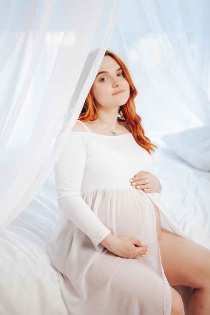 Беременная девушка в белом платье в светлой студии
