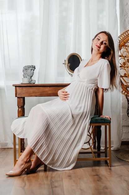 a pregnant girl in a white dress sits at the table