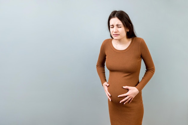 A pregnant girl who has a stomach ache stands on a colored background isolated