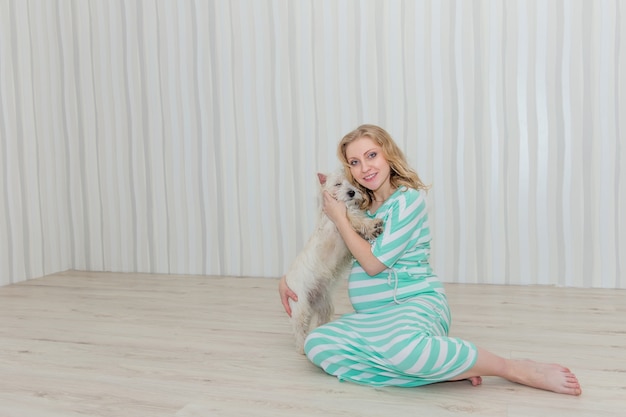 Pregnant girl with a dog in hands sits on the floor