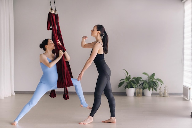 Pregnant girl A woman with a trainer does yoga in a hammock in the gym The concept of a healthy lifestyle motherhood