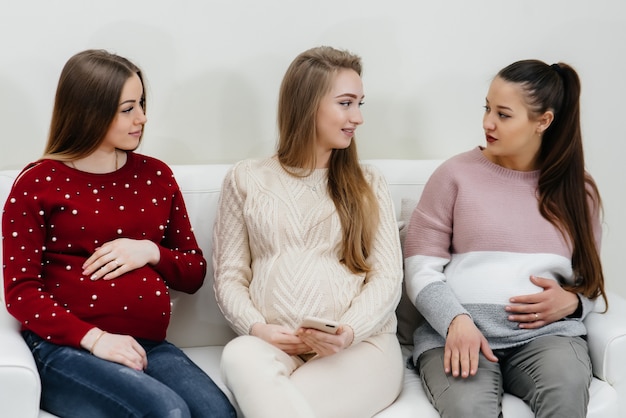 Pregnant girls sit on the couch and have fun chatting with each other. Pregnancy and taking care of the child's future.