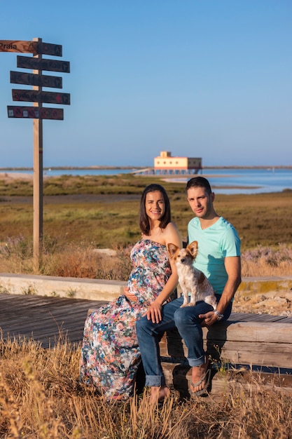 Pregnant happy couple with small dog at beach