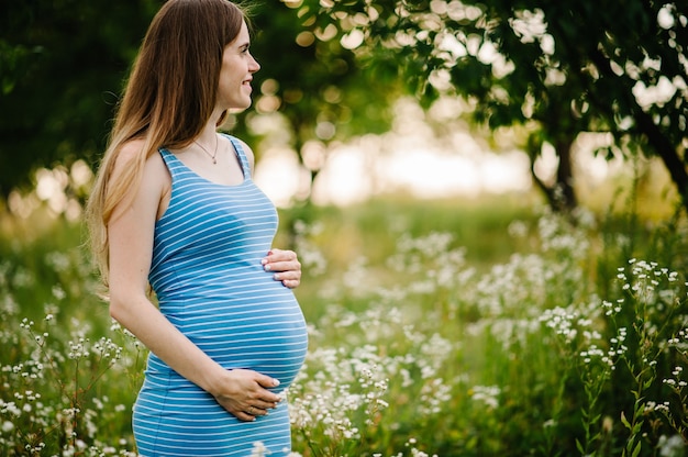 Ragazza incinta felice stare in piedi e tenere le mani sullo stomaco, stare all'aperto nella superficie del giardino con alberi verdi