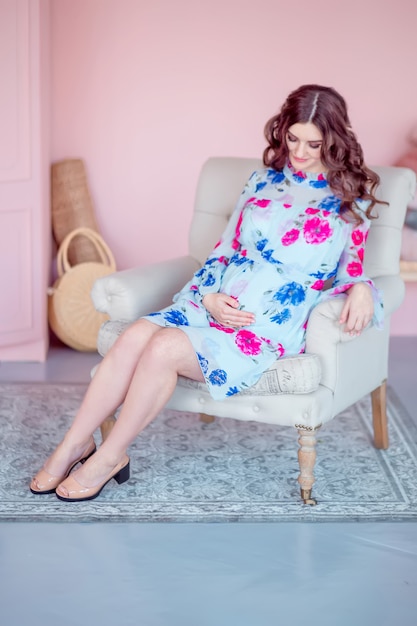 Pregnant happy woman sitting in the chair. Room in pastel pink