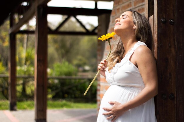 Pregnant Hispanic closes her eyes and enjoys the summer sun a sunflower in his hand