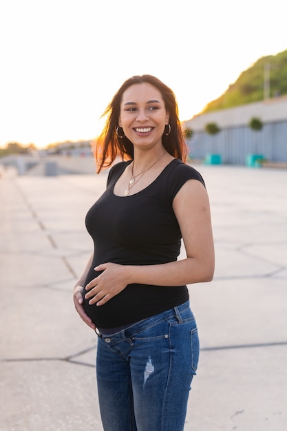 Беременная латиноамериканка в парке, касаясь живота