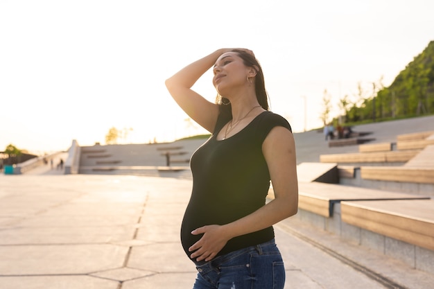 Pregnant hispanic woman in the park, touching belly