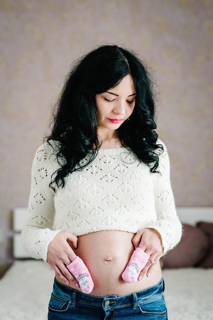 Pregnant holding socks for a baby on stomach and on belly of future daughter at home