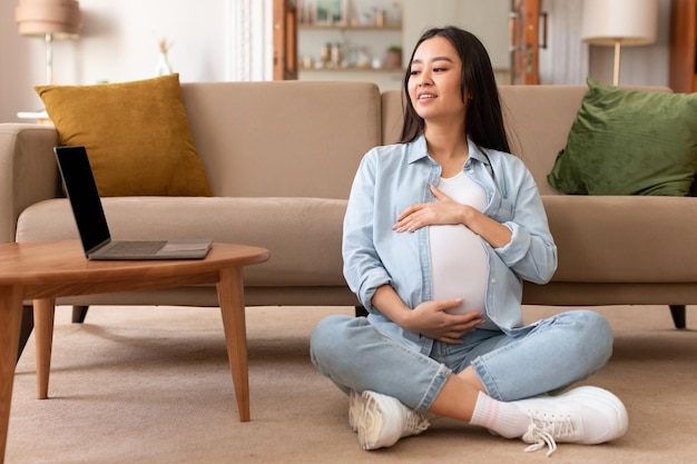 Pregnant japanese lady using laptop working online in living room