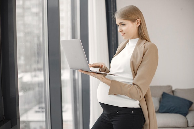 Pregnant lady typing on a laptop while standing in modern office