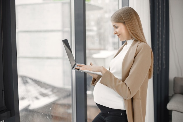 Pregnant lady typing on a laptop while standing in modern office