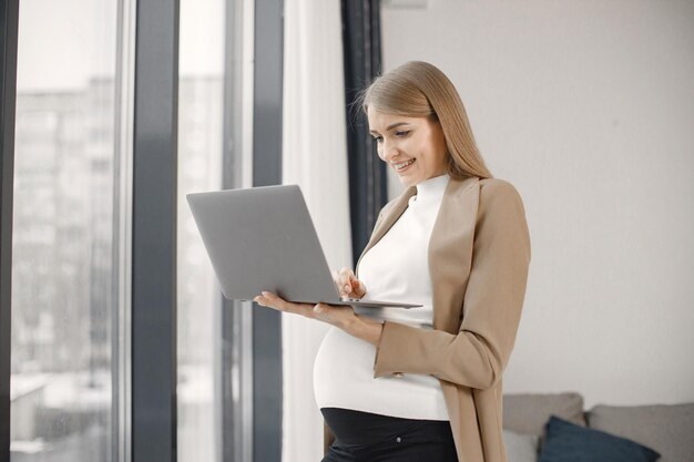 Pregnant lady typing on a laptop while standing in modern office