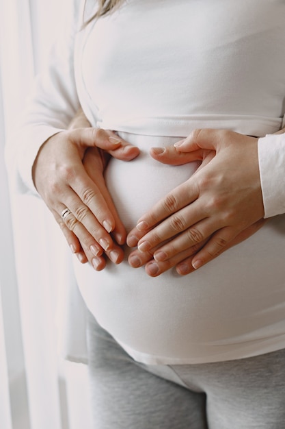 Foto incinta in abiti leggeri. mani sulla pancia di una donna incinta. famiglia dalla finestra.