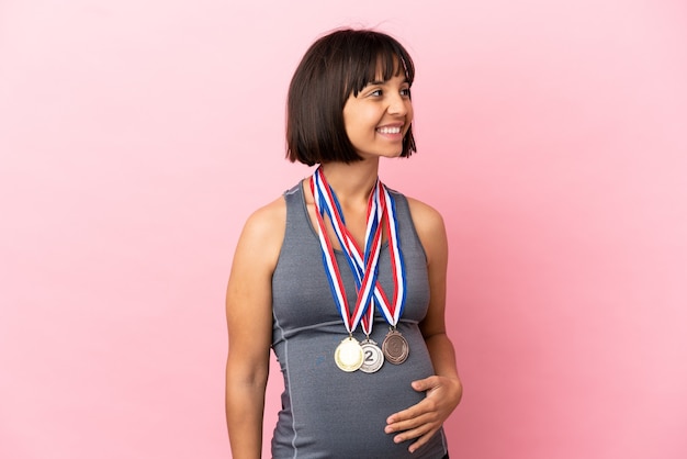 Беременная женщина смешанной расы с медалями, изолированными на розовом фоне, глядя в сторону