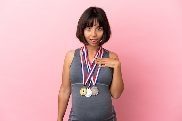 Pregnant mixed race woman with medals isolated on pink background surprised and shocked while looking right