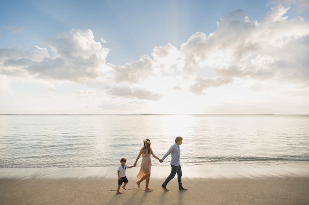 Беременная мать, отец и сын гуляют на пляже
