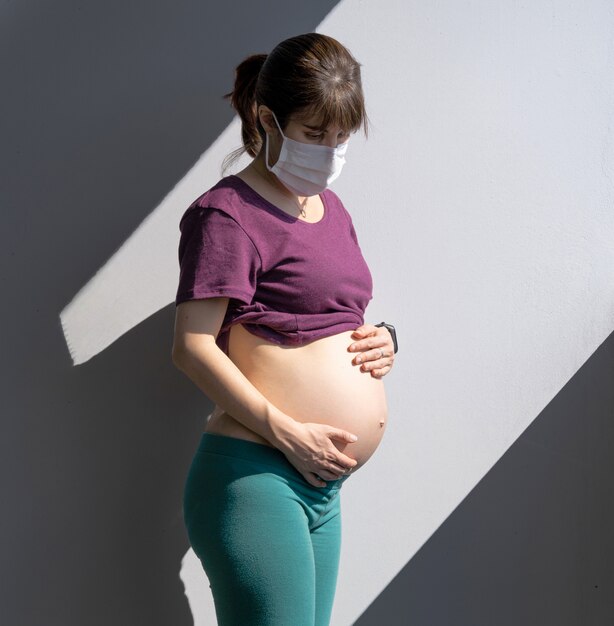 Pregnant protecting herself from coronavirus COVID-19 with a mask and stay in isolation.