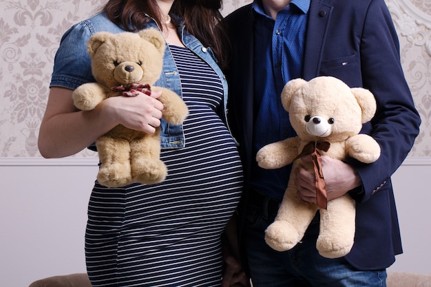 Pregnant wife and husband hold bears in hands