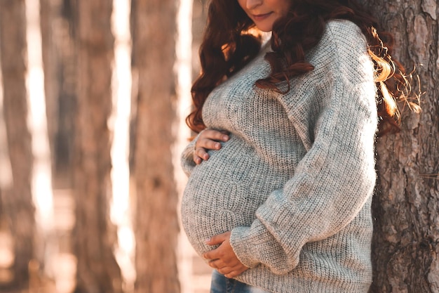 Pregnant woman 30-35 year old wearing warm knitted sweater posing outdoors Motherhood