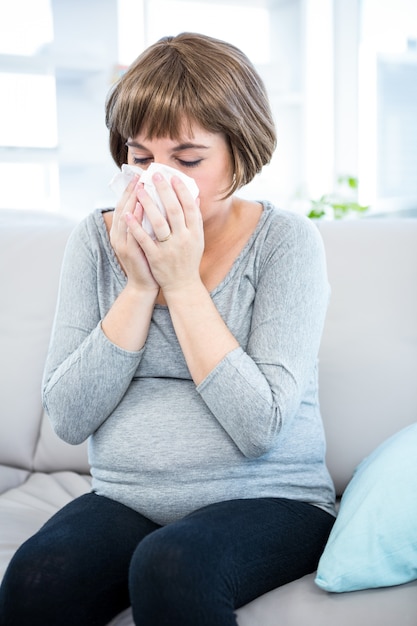 Pregnant woman about to sneeze while sitting on sofa at home