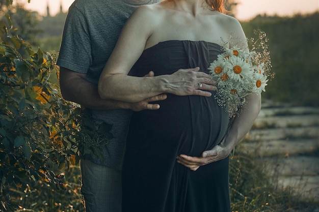 写真 自然に囲まれた外で腹を抱きしめる妊婦と夫妊娠