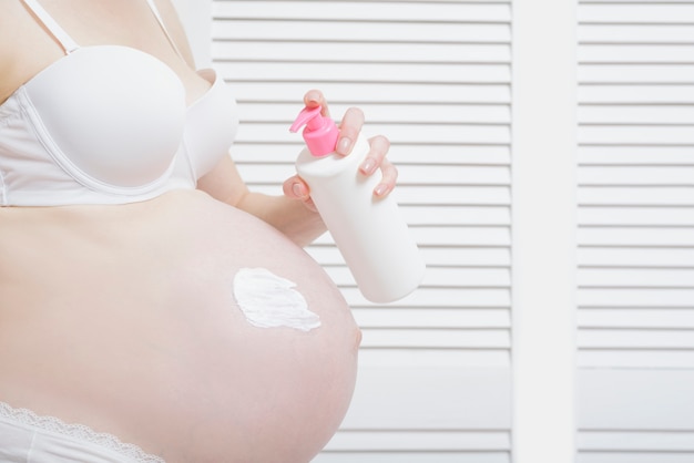 Pregnant woman applies cream on her belly. Close-up