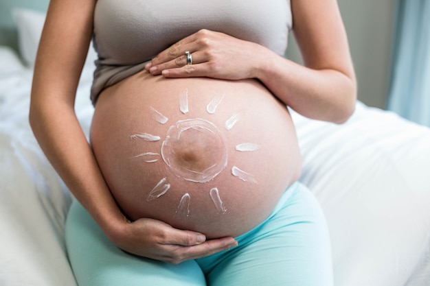 Pregnant woman applying cream on her belly in her bedroom