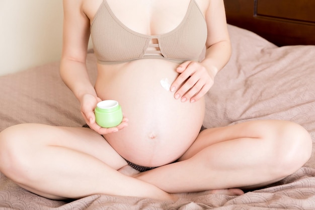 Photo pregnant woman applying stretch mark cream to belly pregnancy people and maternity concept pregnant apply antistretch mark cream on her belly