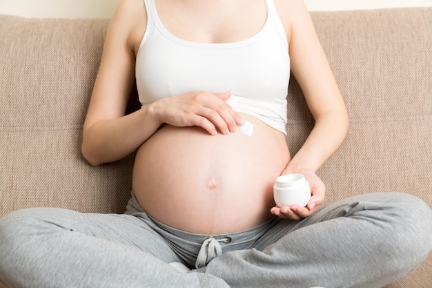 pregnant woman applying stretch mark cream to belly pregnancy people and maternity concept pregnant apply antistretch mark cream on her belly