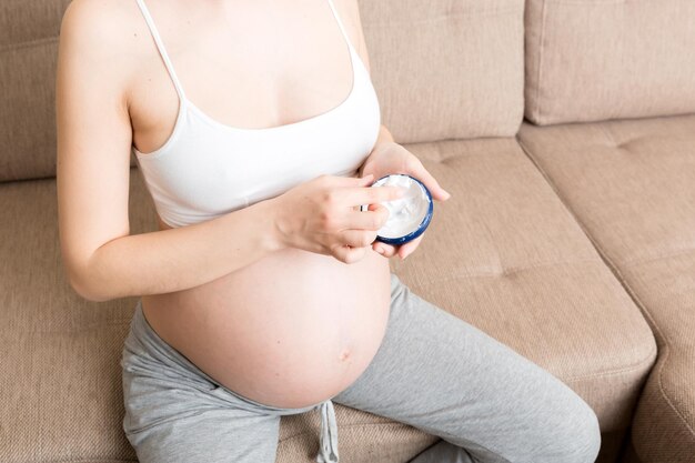 Photo pregnant woman applying stretch mark cream to belly pregnancy people and maternity concept pregnant apply antistretch mark cream on her belly