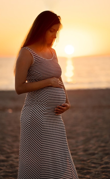 Pregnant woman at beach on background of sea at sunset in eveningFemale silhouette motherHappy maternity motherhood conceptCopyspace