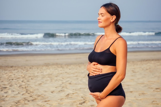 Donna incinta sulla spiaggia che fa yoga.