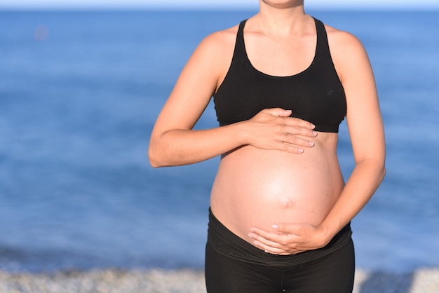 Pregnant woman beach - hands in heart shape on belly