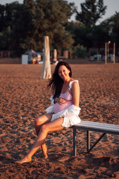 해변에서 임산부 핑크색 수영복과 흰색 수영복을 입은 매력적인 다리가 많은 임산부를 웃고 있습니다.