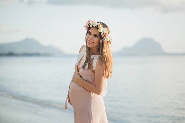 Беременная женщина в красивом платье на берегу океана.