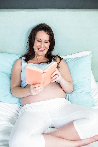 Pregnant woman on bed reading a book at home 